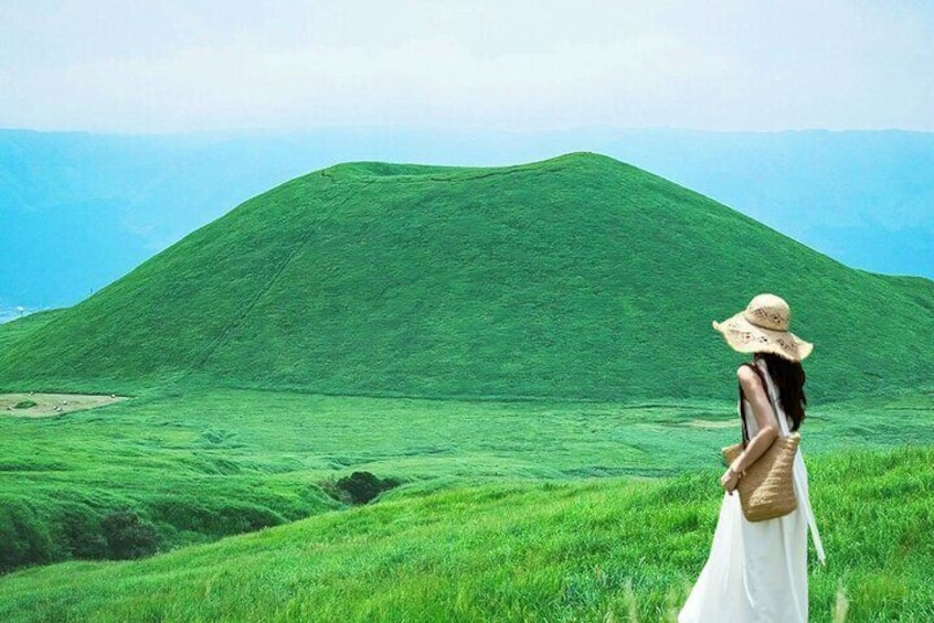 Una persona con un abito bianco e un cappello di paglia in piedi su una collina erbosa con vista su un paesaggio verde. 1