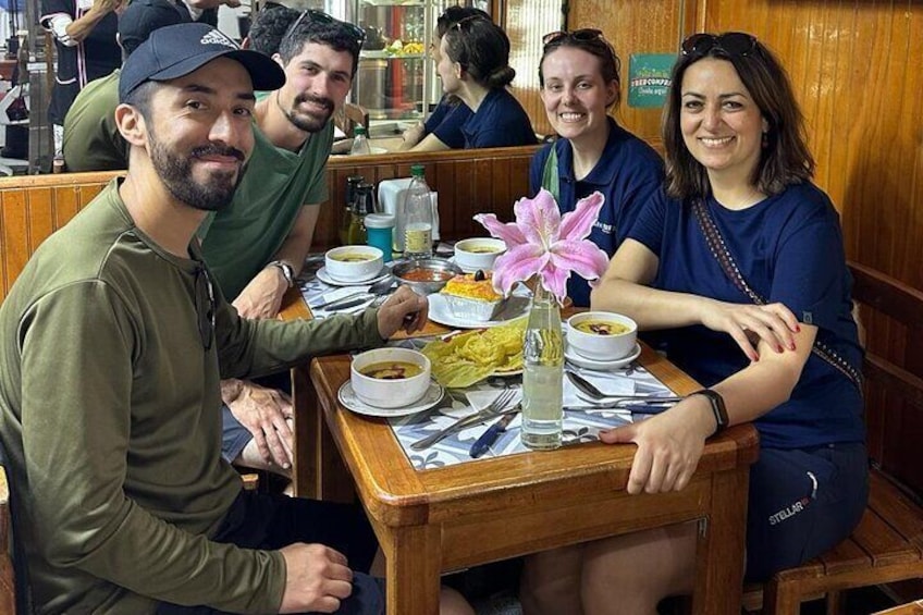 A group of people dining at a restaurant with wooden booths and a table set with bowls, plates, and a vase with a pink flower. 1