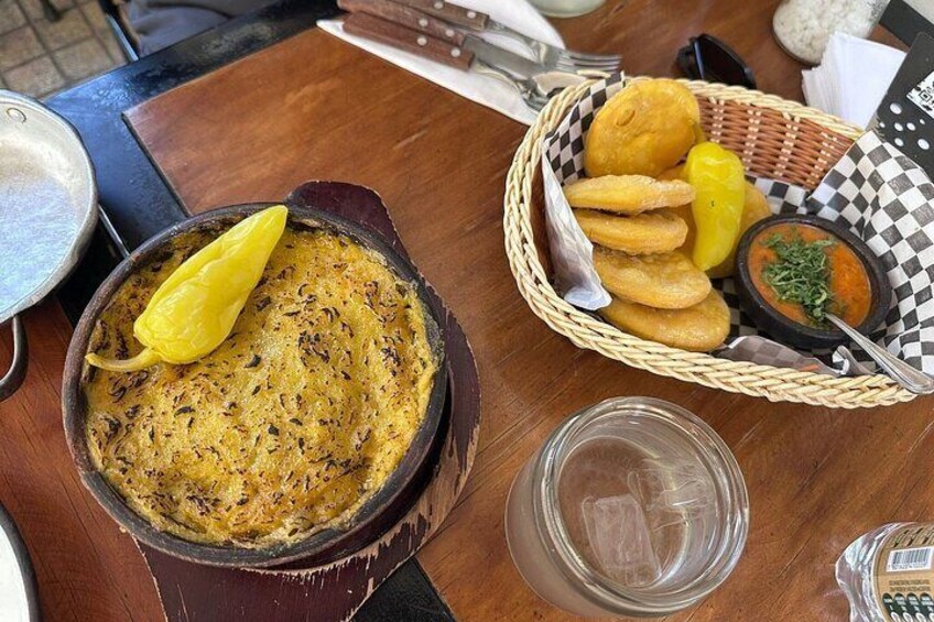 A dish of yellow curry with a lemon wedge, a basket of fried snacks, and a small bowl of sauce on a wooden table. 3