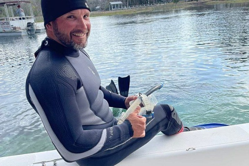 A person in a wetsuit sitting on a boat, holding a fishing rod. 5
