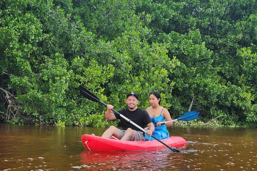 Zwei Personen paddeln mit ihren Kajaks auf einem Fluss, umgeben von dichtem Grün. 1