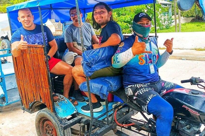 Eine Gruppe von Personen in einem motorisierten Wagen mit blauem Verdeck, eine Person zeigt Daumen hoch, und ein Motorrad mit sichtbarem Motor. 4