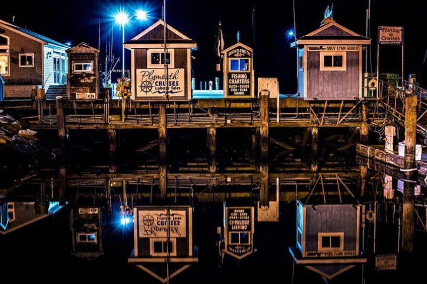 A waterfront with illuminated buildings and signs, including 'Plymouth Cruises' and 'Fishing Charters.' 2