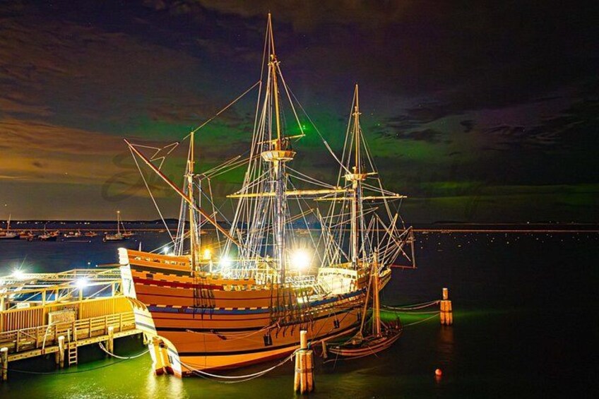 A large sailing ship docked at a pier with a colorful aurora display in the background. 3