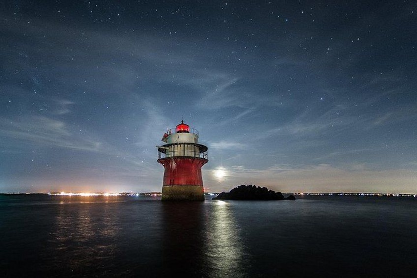 A lighthouse at night with a full moon in the background and a small island to the right. 1