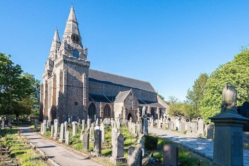 Una iglesia histórica con una aguja alta, rodeada por un cementerio con lápidas. 1
