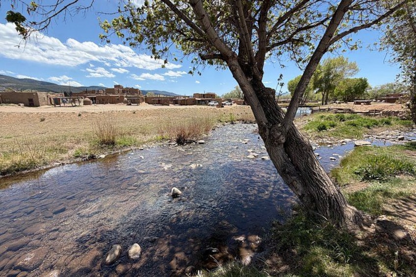 A river with clear water, a tree, and a distant building complex. 4