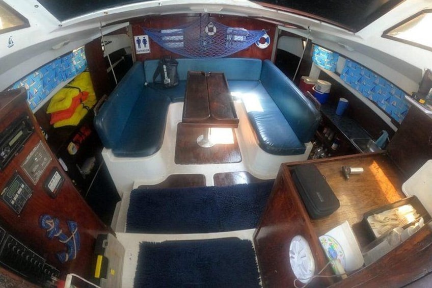 A boat's interior with a blue cushioned seating area, a wooden table, and a control panel. 3