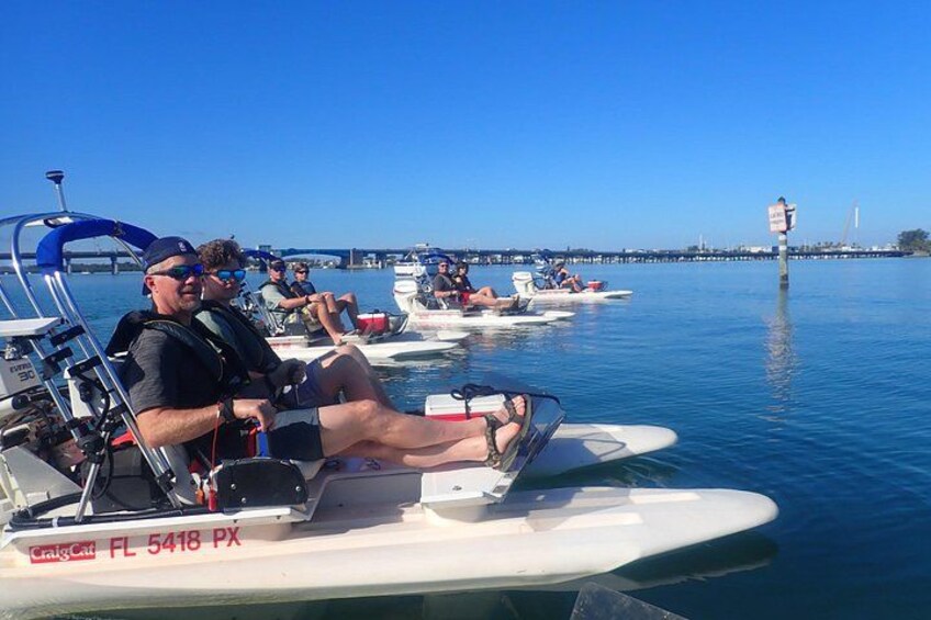 A group of people on paddle boats on a calm body of water with a bridge in the background. 2