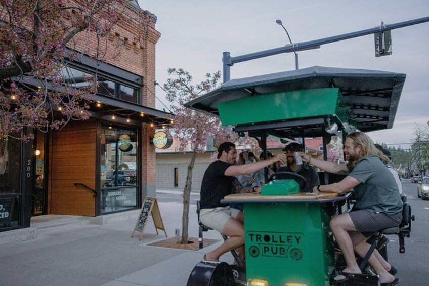 A green trolley with 'TROLLEY PUB' written on it, parked on a street with people interacting at the front. 2