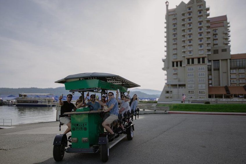 A green trolley with passengers, a body of water, and a tall building in the background. 3