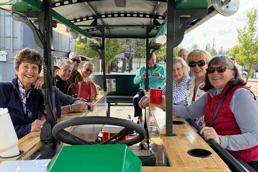 A group of people on a green trolley, with a steering wheel and a wooden bench. 5