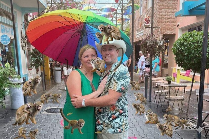 Et par omfavner under en regnbuefarvet parasol, omgivet af flere aber. 1