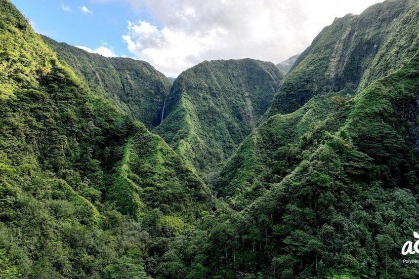 A lush valley with steep, forested mountains and a waterfall. 2