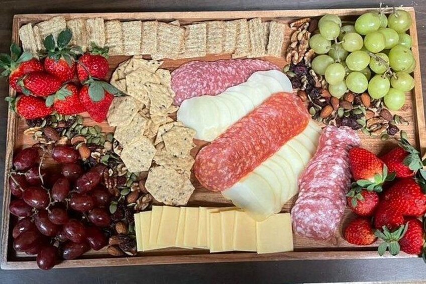 A wooden board with various cheeses, crackers, grapes, and sliced meats. 3