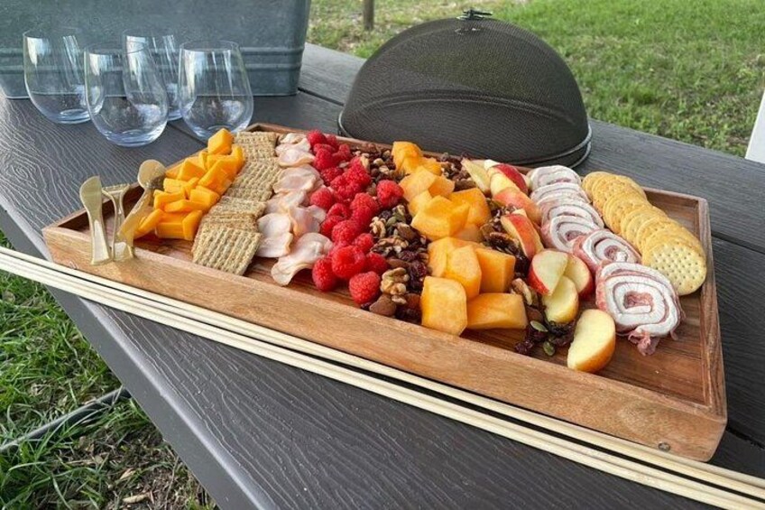 A wooden tray with various cheeses, fruits, and crackers on an outdoor table. 5