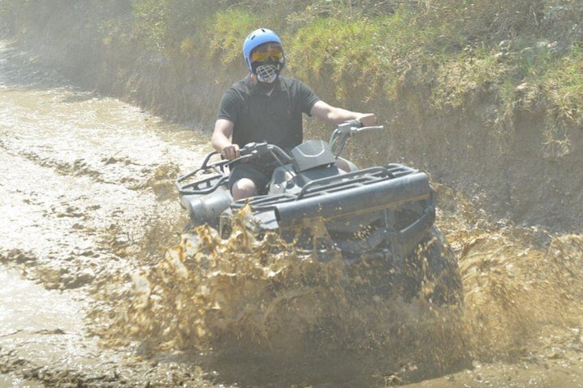 A person riding an ATV through a muddy water crossing. 5