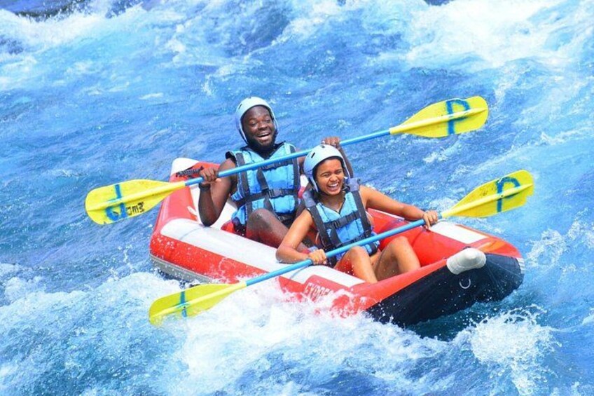 Two people in a red inflatable raft with yellow paddles, navigating through white water rapids. 2