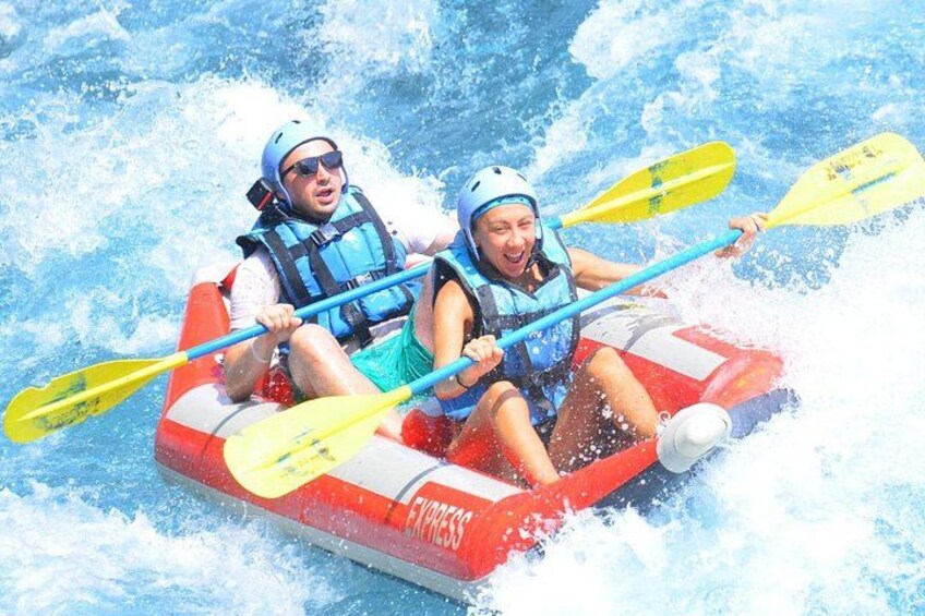 Two people in a red inflatable raft with paddles, navigating through white water rapids. 3
