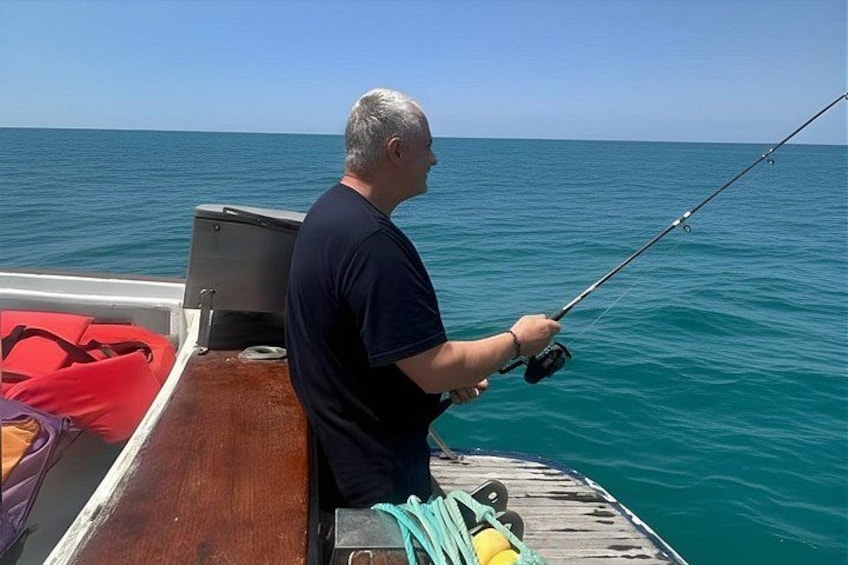 A man fishing on a boat with calm sea water and a clear sky. 5
