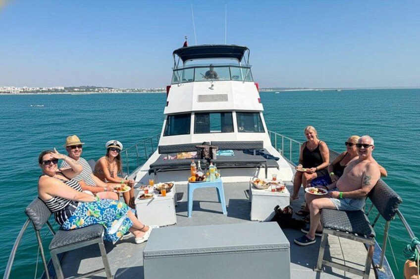 A group of people on a boat with a table set up in the middle, surrounded by water. 1