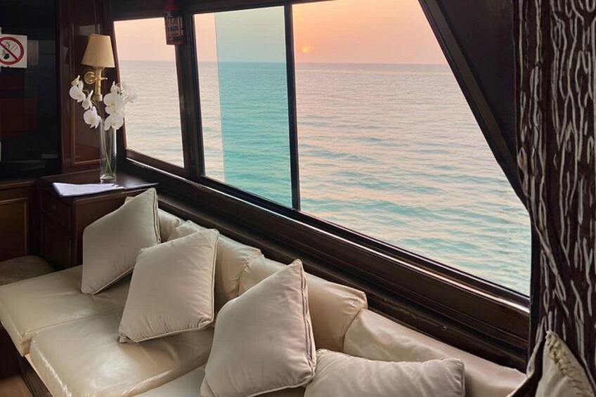 A cabin with a sofa, a vase with flowers, and a view of the ocean at sunset. 2
