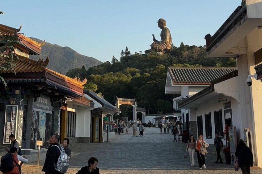 Una calle tradicional china con gente caminando, una gran estatua de Buda en una colina y edificios tradicionales. 2