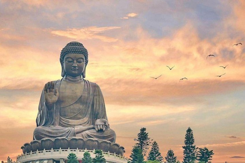 Una gran estatua de Buda sentado sobre una base circular, rodeado de árboles y un cielo nublado. 1