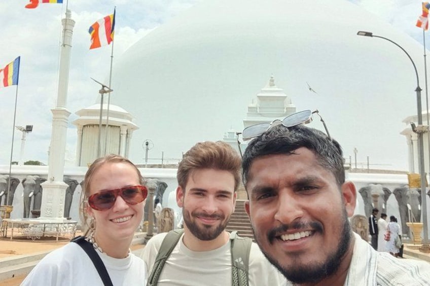 Three people in front of a large white dome structure with flags. 2