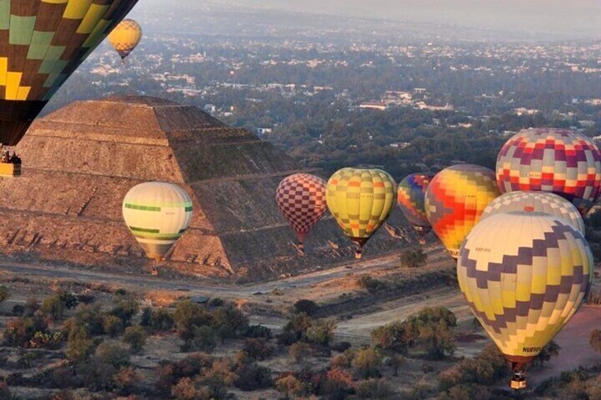A group of colorful hot air balloons over a desert landscape with a pyramid in the background. 1