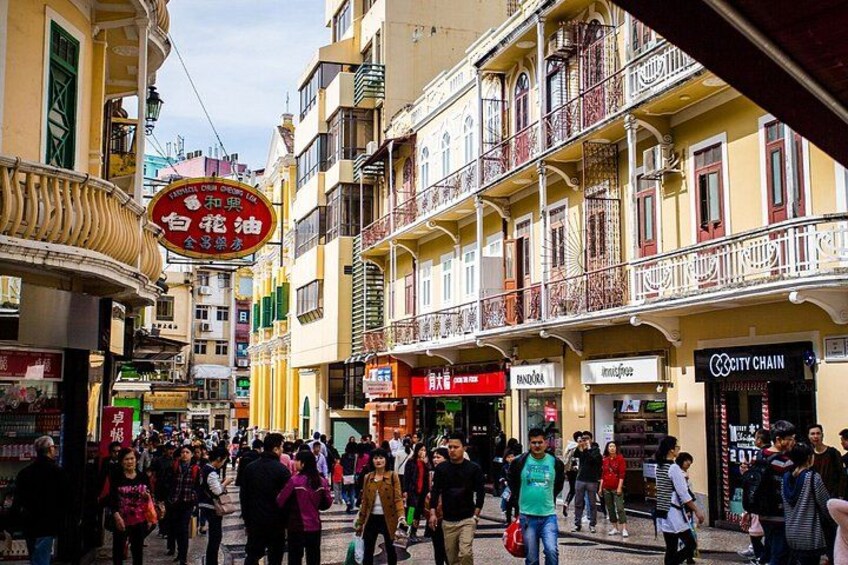 Une rue animée, bordée de piétons, de boutiques et d’immeubles à plusieurs étages dotés de balcons. 3