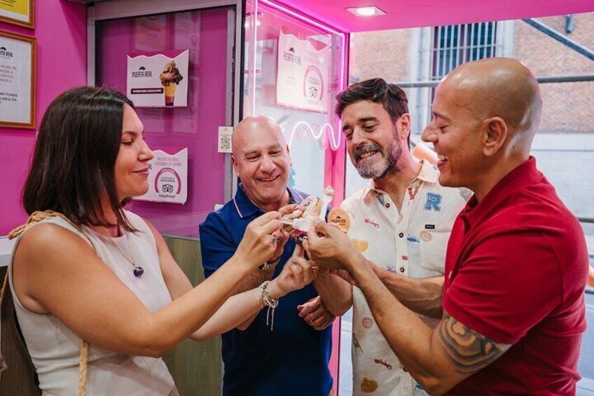 A group of people in a pink-themed indoor setting, possibly a shop or cafe, with a menu board and a neon sign. 2