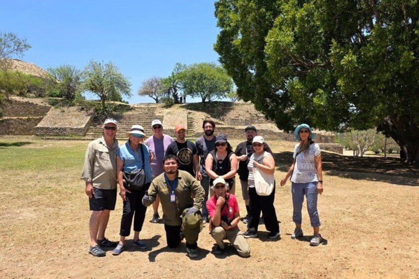 A group of people standing in a dry, grassy area with trees and a hill in the background. 5