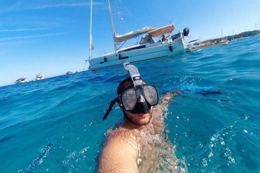 A person snorkeling in clear blue water with a sailboat in the background. 1