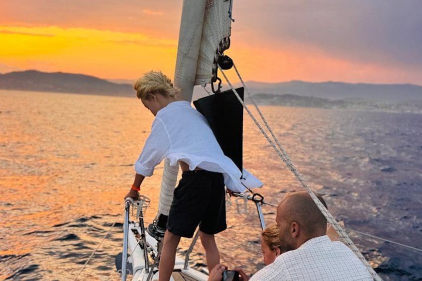 A sailboat with a person standing on the deck, another person seated, and a third person leaning over the side. 2