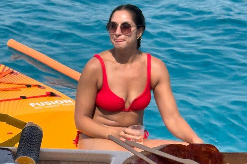 A person in a red bikini sitting on a boat with a paddleboard labeled 'FUSION' in the background. 3