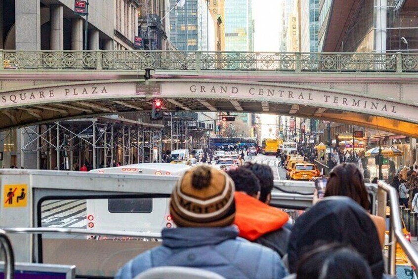 A busy street scene with a bridge labeled "SQUARE PLAZA GRAND CENTRAL TERMINAL" and a crowd of people waiting for transportation. 4