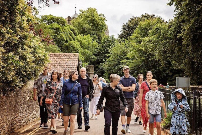 A group of people walking on a path surrounded by greenery and stone walls. 1