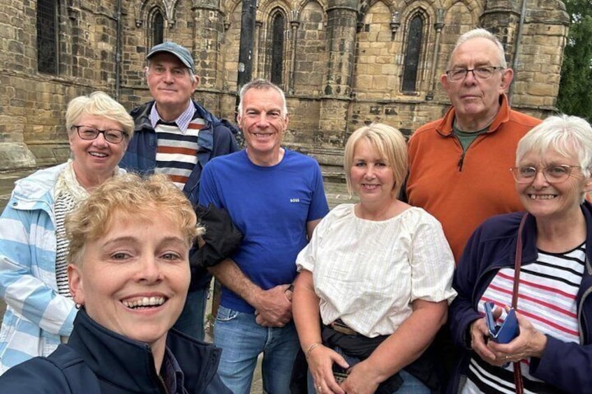 A group of people in front of a historic stone building with arched windows and detailed stonework. 2