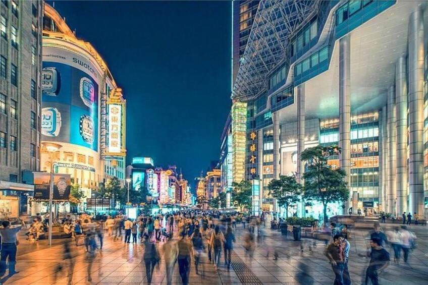A bustling urban square at night with illuminated buildings and a crowd of people. 1