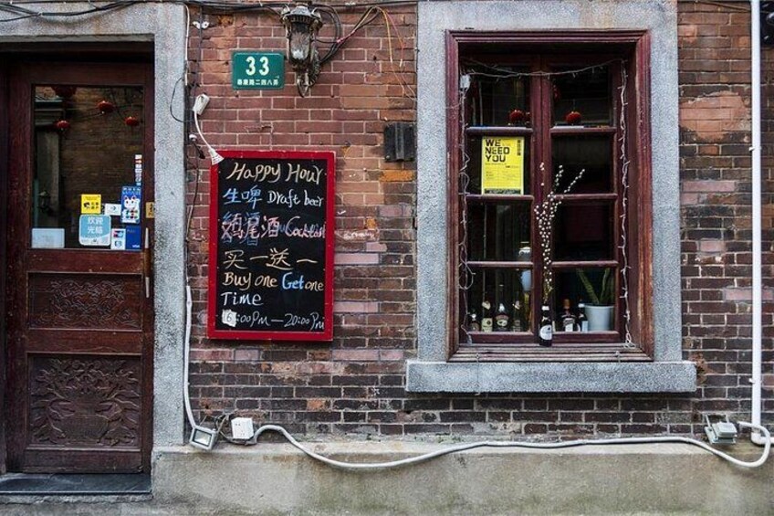 A brick building with a window displaying bottles, a door with a sign, and a chalkboard sign advertising a happy hour. 2