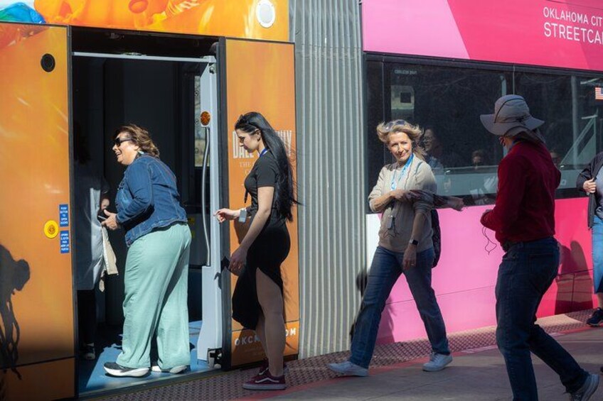 People exiting a brightly colored bus with 'OKLAHOMA CITY STREETCAR' written on it. 2