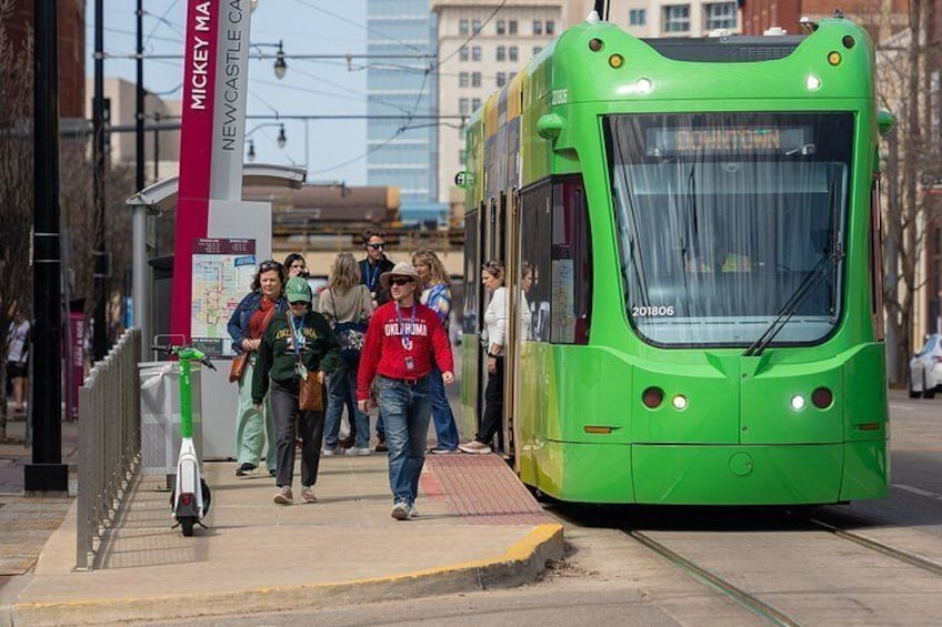 A green tram on a city street, people walking on the sidewalk, and a red sign with 'MICKEY CASTLE' text. 4