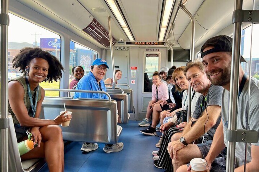 A bus interior with passengers seated, a door with a sign, and a window showing a building outside. 2