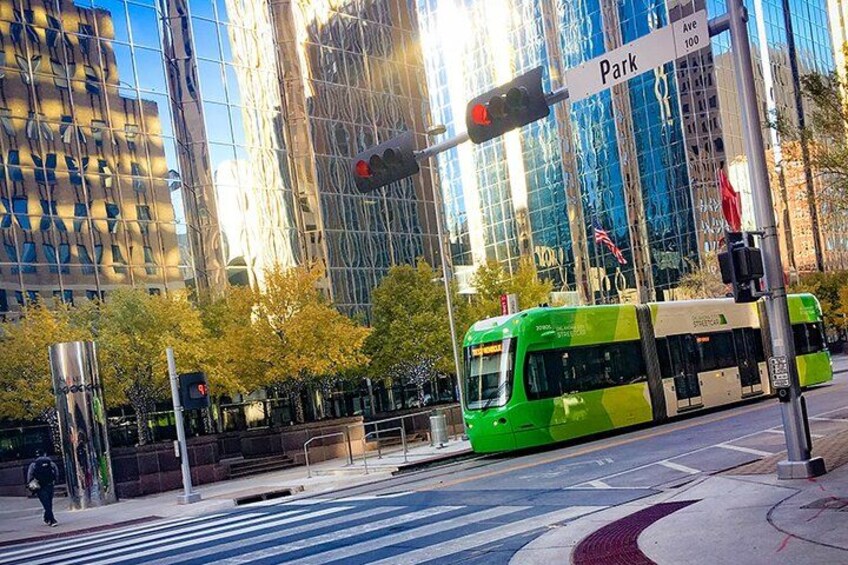 A green tram at a crosswalk with a 'Park Ave 100' sign in the background. 1