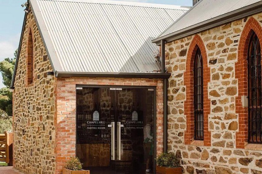 A stone building with a metal roof, a glass door, and a sign indicating a tasting room. 1