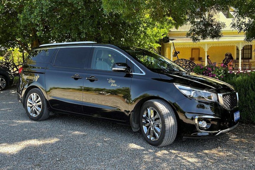 A black SUV parked on a gravel driveway with trees and a building in the background. 2