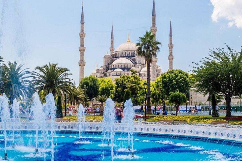 A mosque with four minarets, a fountain, and palm trees. 1