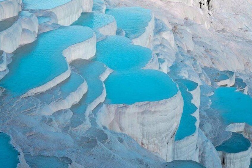 Terraced pools of turquoise water, white travertine formations, and a few people in the distance. 3