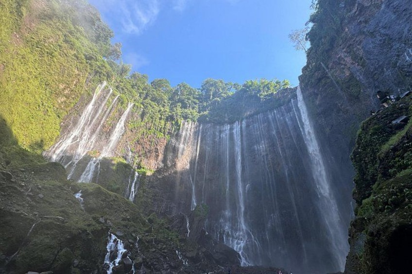 A multi-tiered waterfall cascading down a rocky cliff surrounded by lush greenery. 5